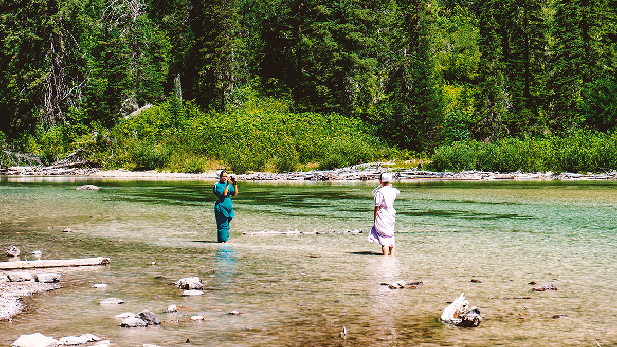 2 women in full dresses stand in a lake to pose for a photo