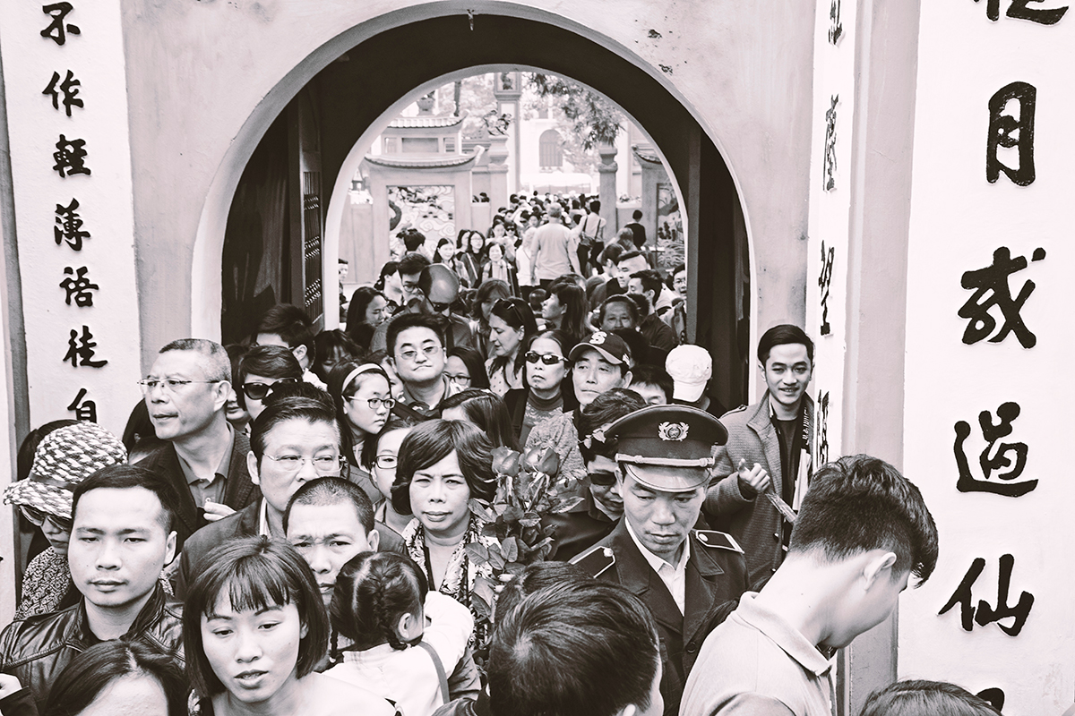 An array of people crowding across a bridge, underneath a circular opening