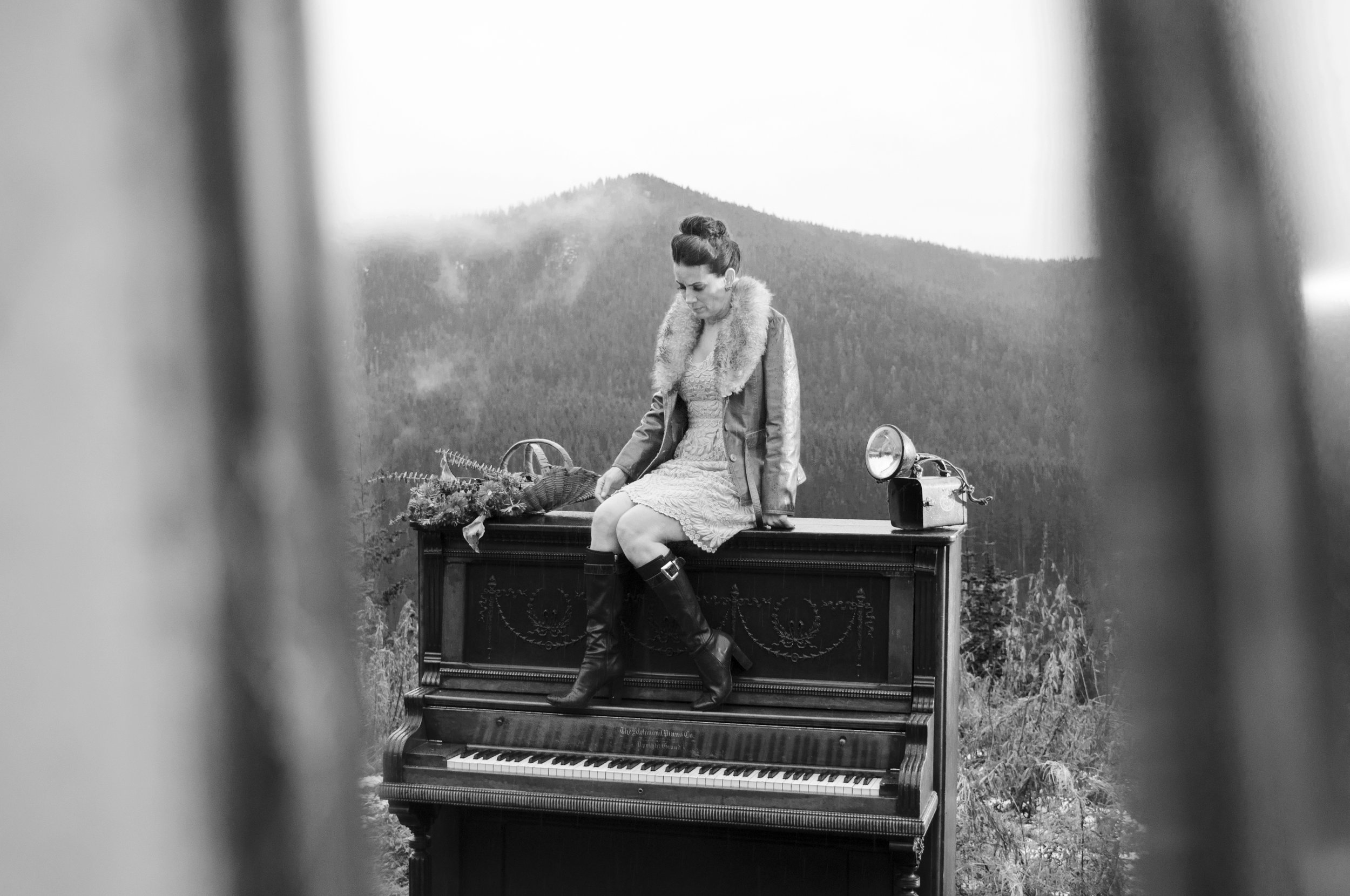 Woman posing on top of a piano with a natural backdrop